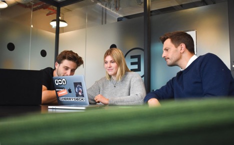 Three digital marketing employees look at a strategy for a client on a Macbook.